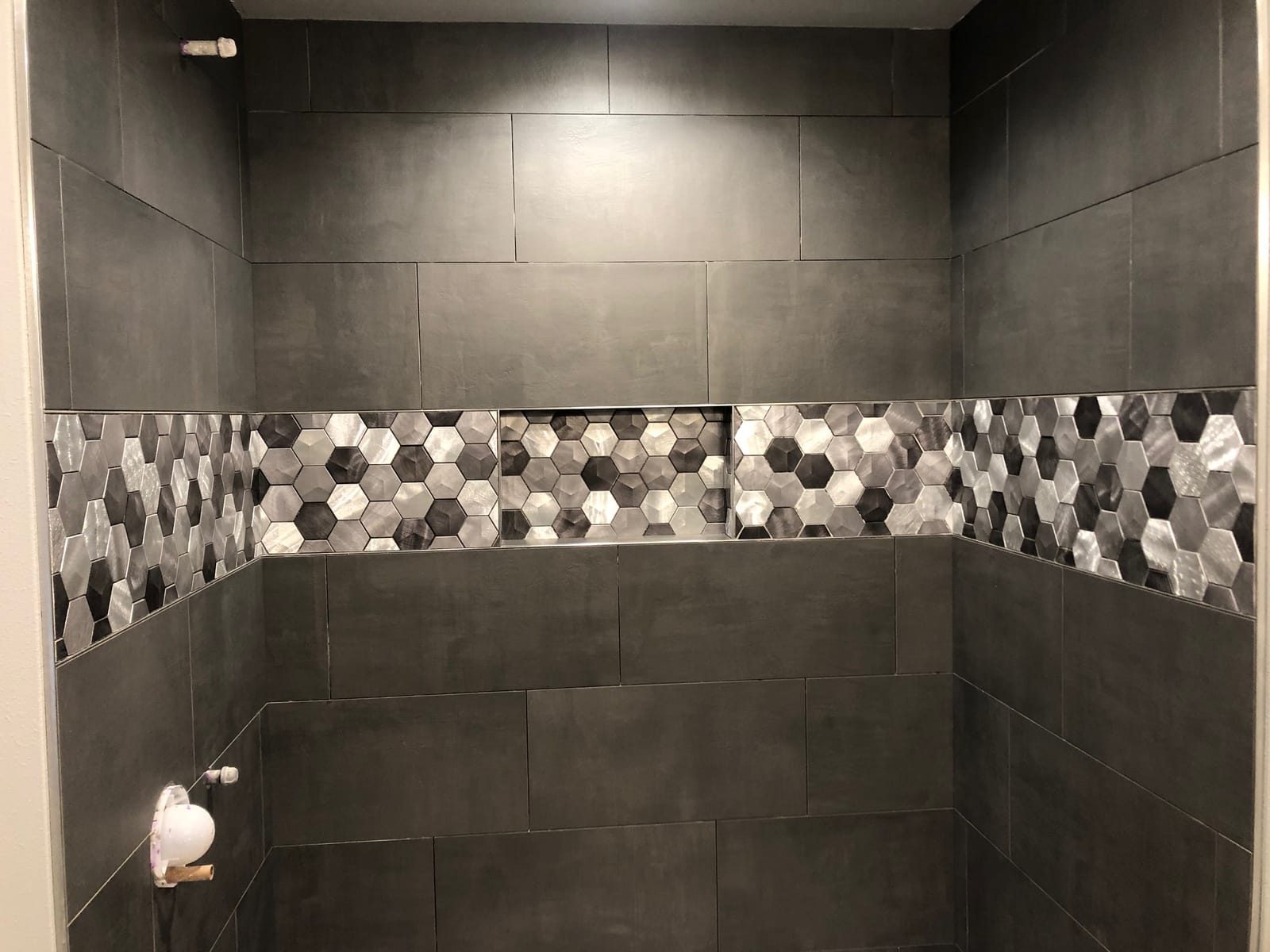 Shower with large dark tile and a metallic hexagon accent band