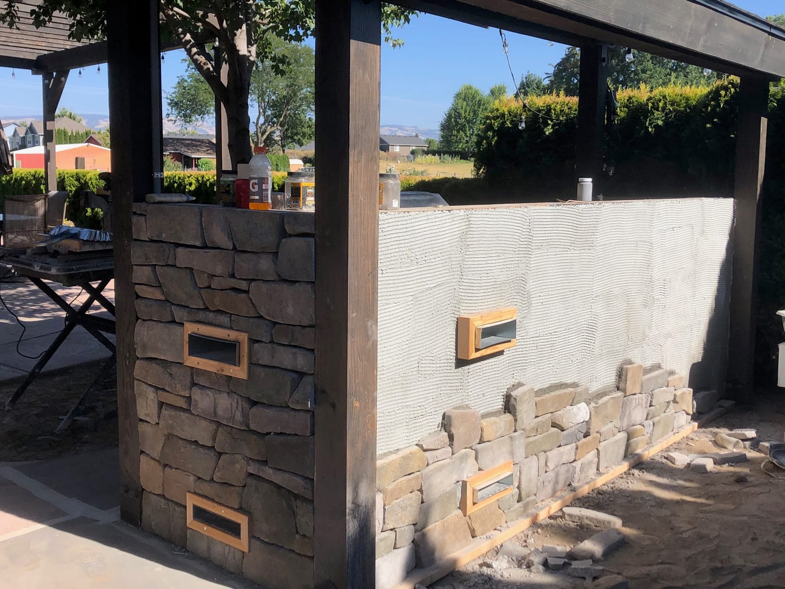 Outdoor bar wall with stone veneer partially installed under a pergola