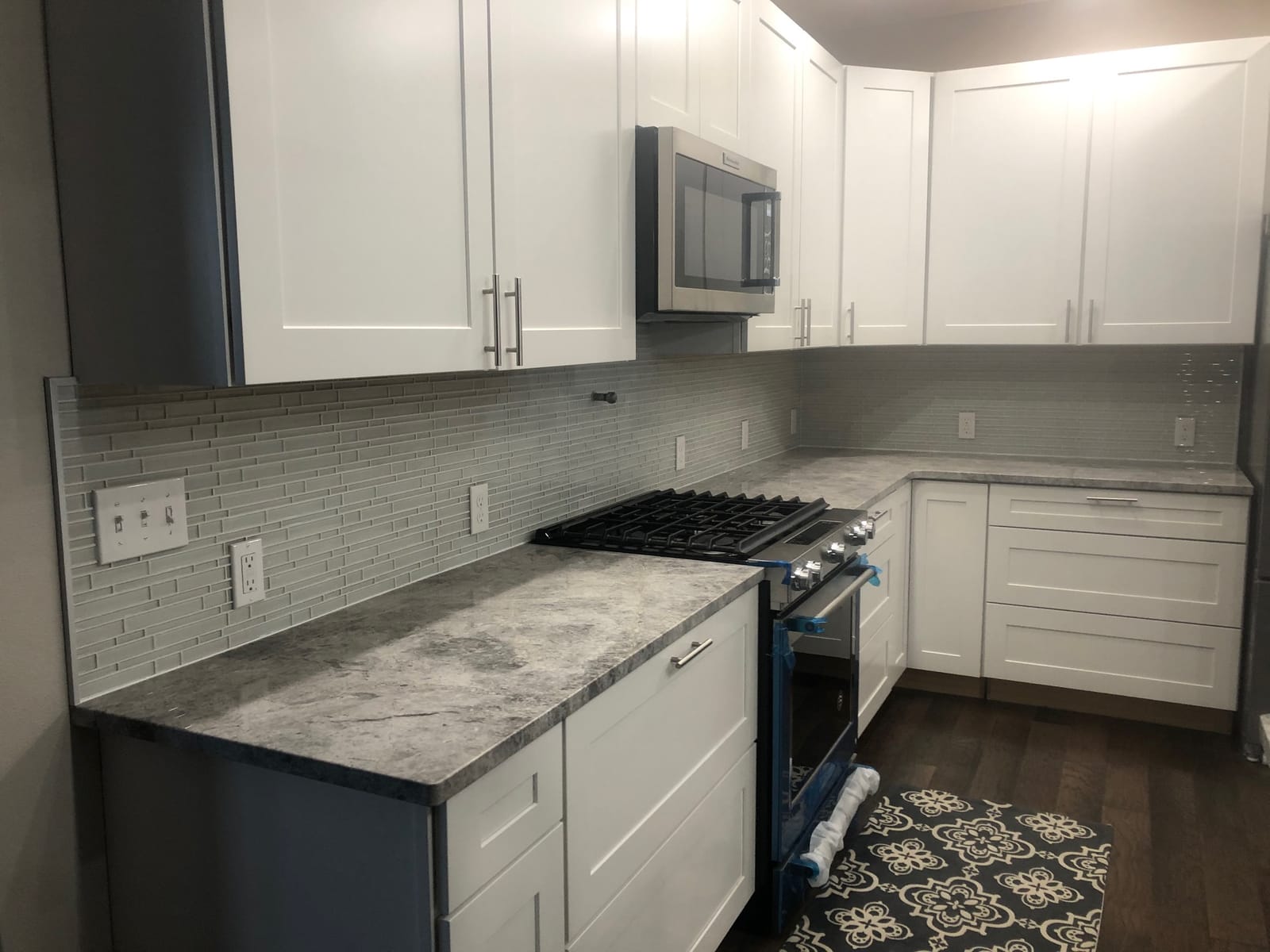 Kitchen with white shaker cabinets, granite counters, and glass tile backsplash