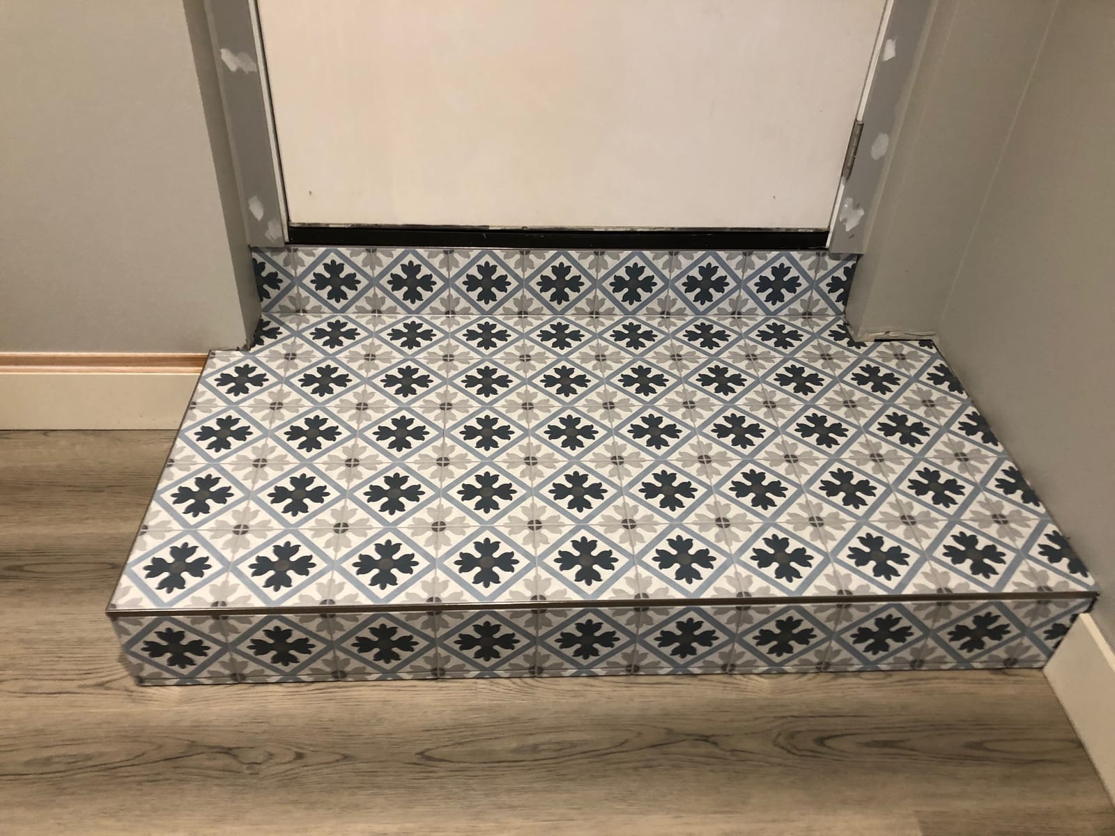 Entry step finished in patterned tile beside wood-look flooring