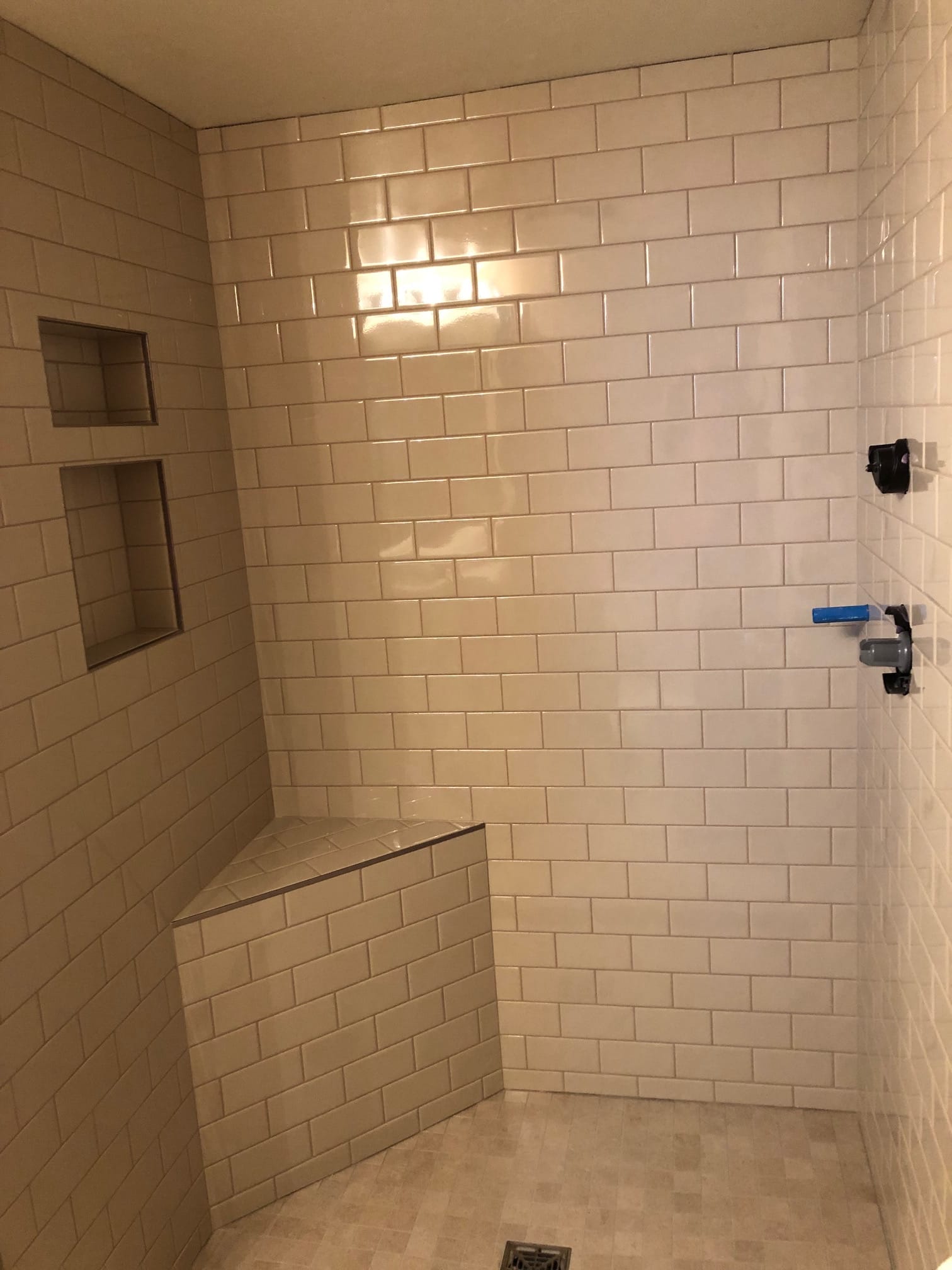Walk-in shower with subway tile, corner bench, and inset niches