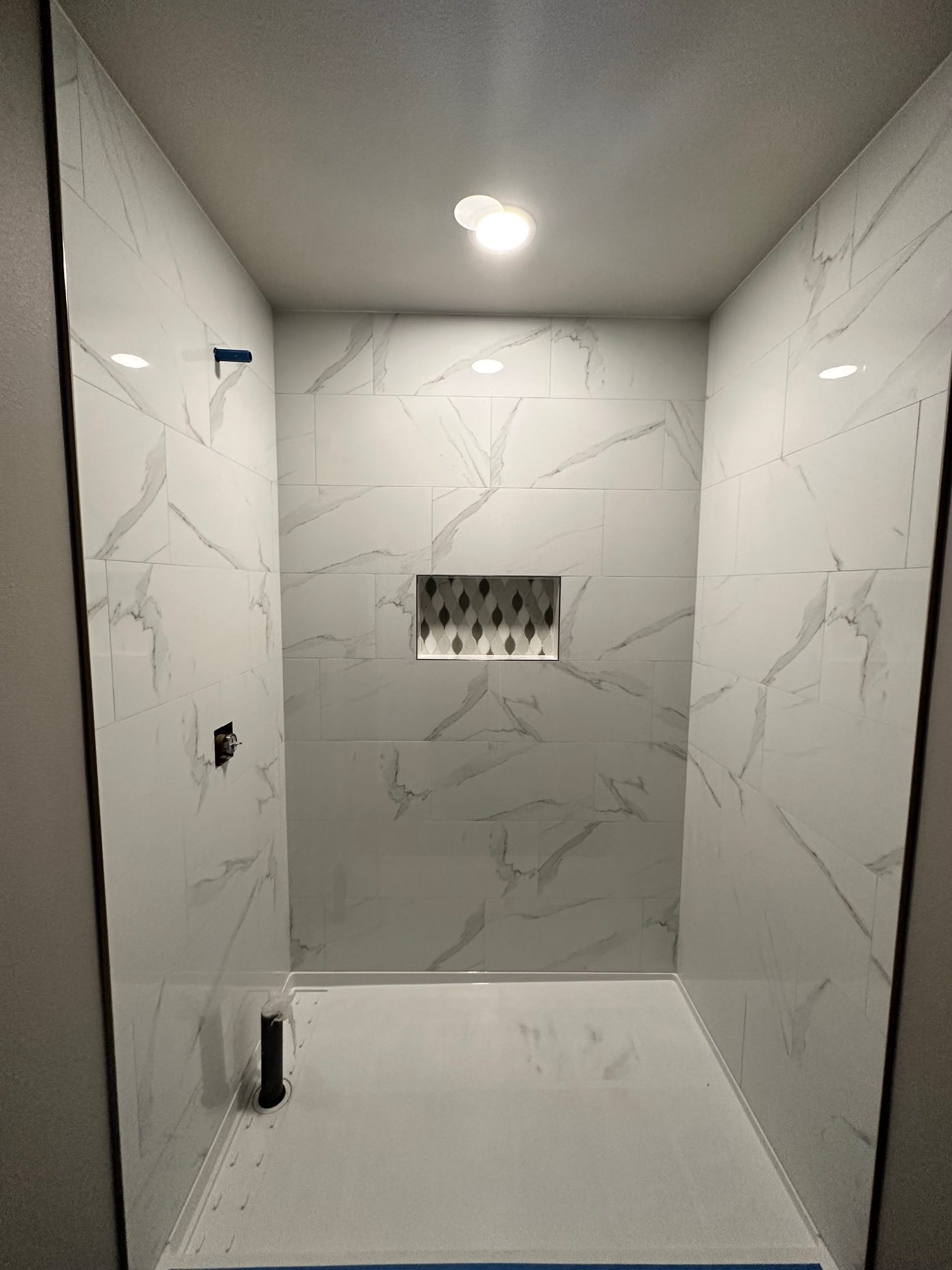 Walk-in shower with marble-look tile and mosaic niche