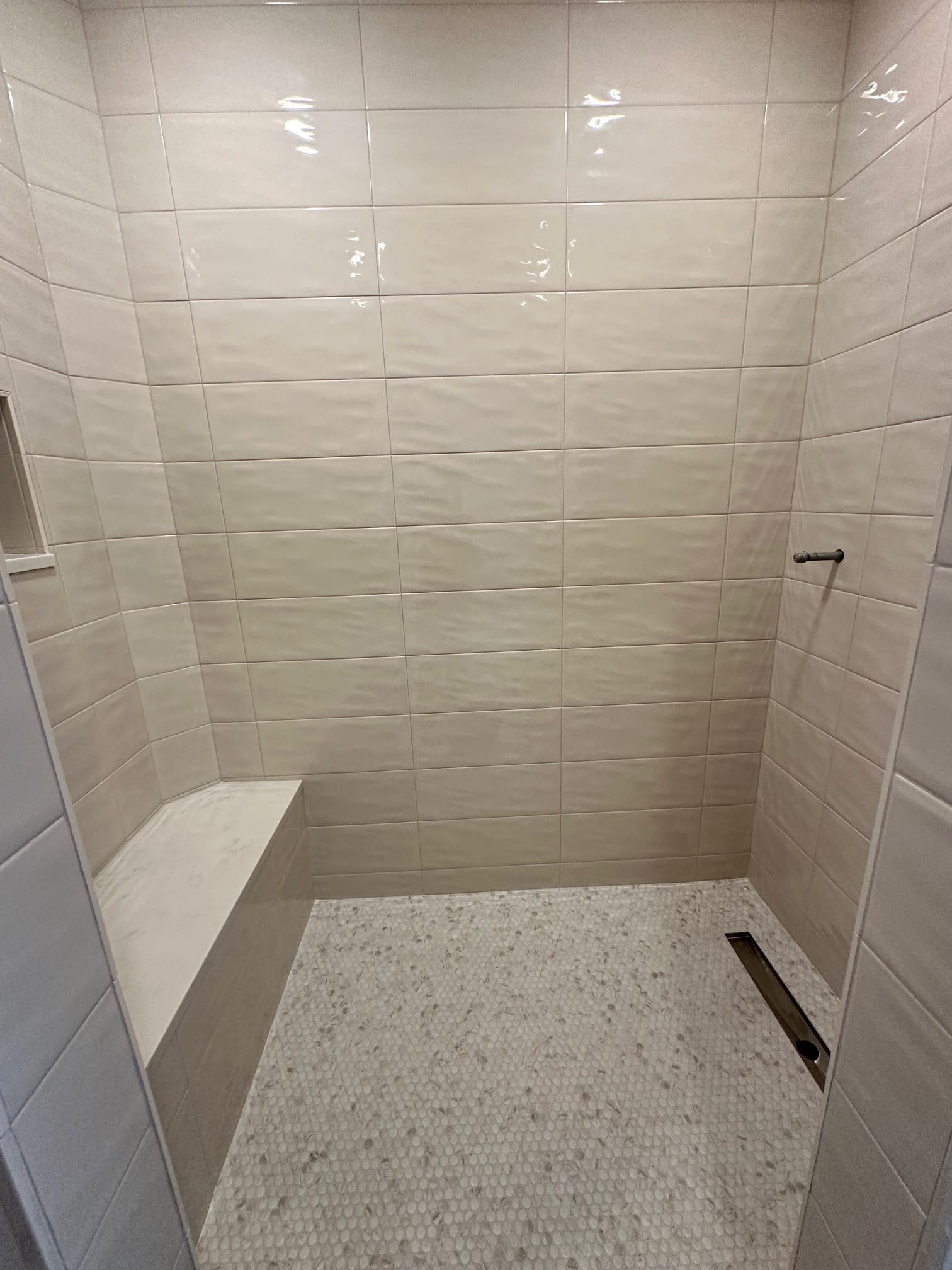 Walk-in shower with wavy ceramic tile, bench, and penny-tile floor