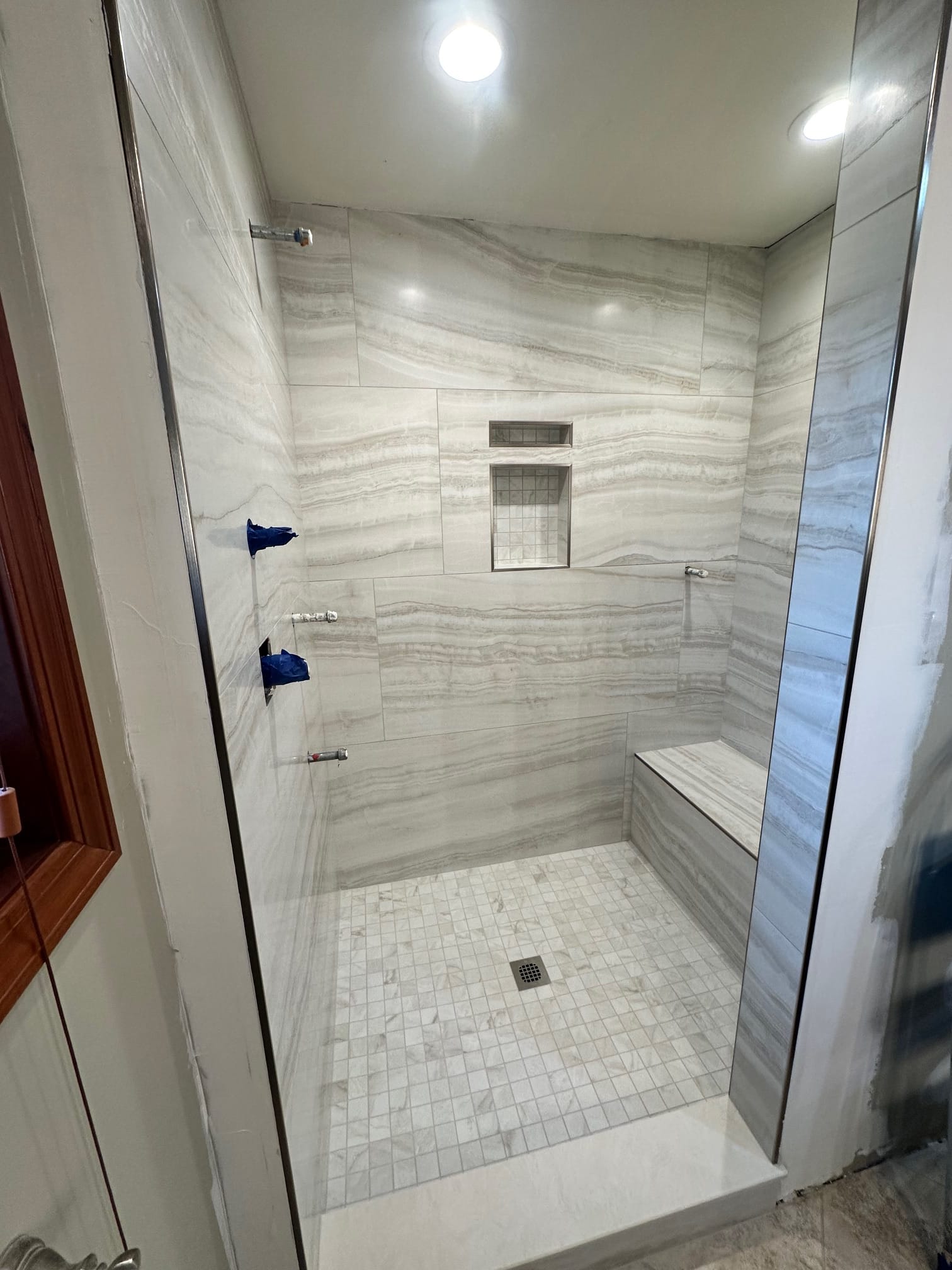 Finished walk-in shower with marble-look tile and built-in bench