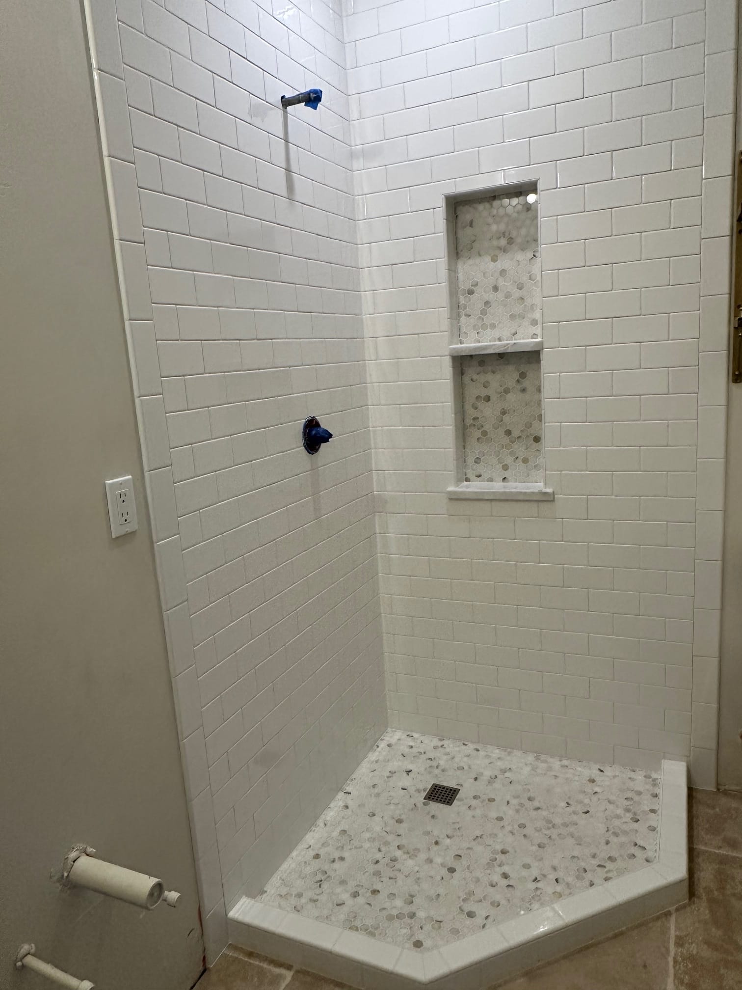 Finished corner shower with white subway tile and hex mosaic floor